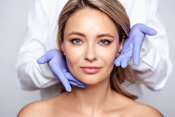 Botox-Doctor Close up of a woman's face with a doctor wearing rubber gloves standing behind her holding his hands around her face to show the amazing Botox Cosmetic treatment from Healthy Aging Medical Centers of New Jersey in Northern New Jersey.