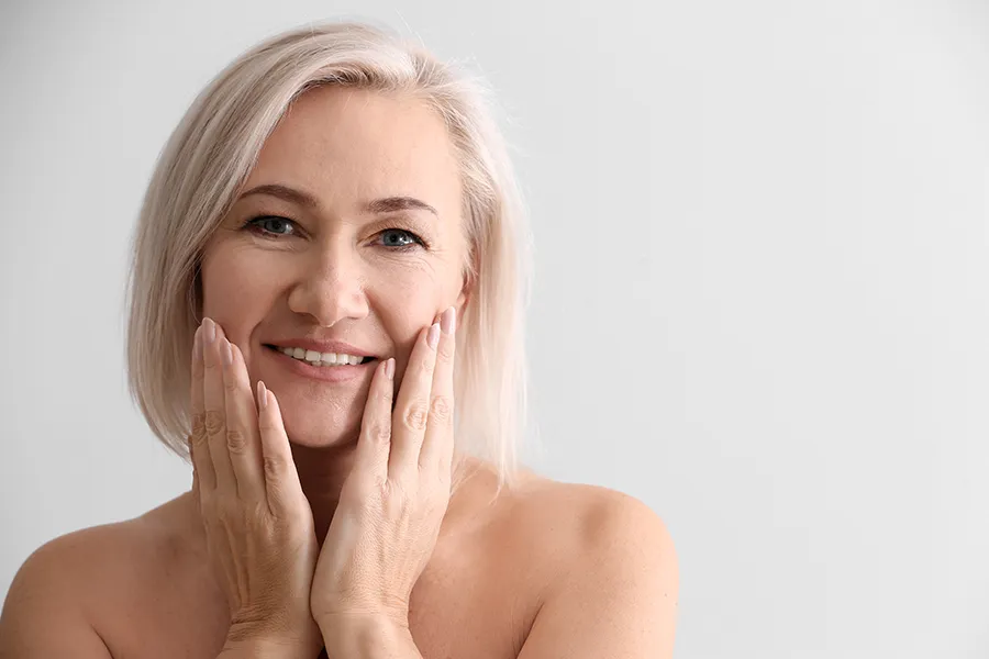 PRP-Microneedling-Clinic A mature woman touches her faces to feel the successful results of PRP microneedling and skin rejuvenation treatments from Healthy Aging Medical Centers of New Jersey in Northern New Jersey.